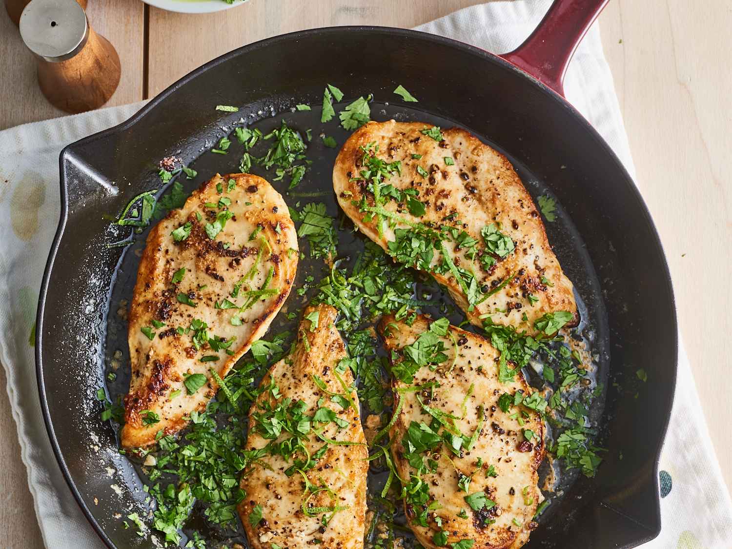 Golden seared chicken breasts in a skillet topped with fresh cilantro and lime wedges